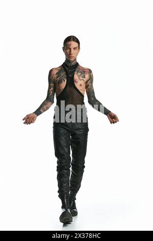 Ein stilvoller Mann voller Tattoos, der selbstbewusst in einem weißen Studio hinuntergeht. Stockfoto