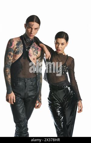 Ein junger, stilvoller Mann und eine Frau mit Tattoos stehen in einem Studio vor grauem Hintergrund zusammen. Stockfoto