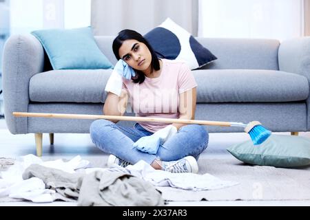 Frau, gelangweilt und Porträt im Wohnzimmer für die Reinigung im Haus mit dreckiger Kleidung und Besen. Genervt, frustriert und launisch von der Hausarbeit Stockfoto
