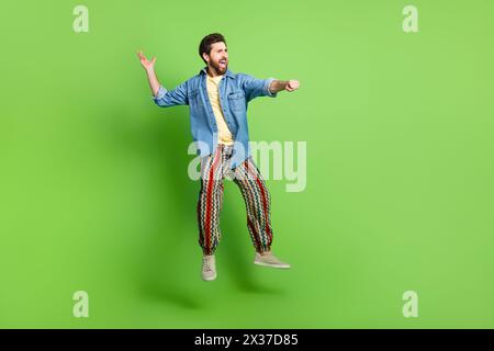 Foto in voller Länge von positivem funky Guy gekleidetem Jeans-Hemd, das hoch aufstehendes Pferd springt leerer Raum isolierter grüner Farbhintergrund Stockfoto