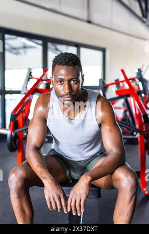 Männlicher afroamerikanischer Athlet und Fitnessmodell ruhen während der Trainingspause im Fitnessstudio aus Stockfoto