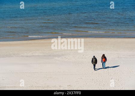 In der Nebensaison spazieren ein paar Reisende in warmer Kleidung mit Rucksäcken entlang eines einsamen Strandes in der Nähe des Meeres. Kurische Nehrung, Neringa, Litauen Stockfoto