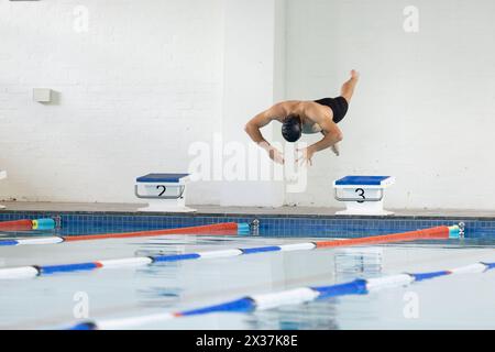 Kaukasischer junger männlicher Schwimmer taucht in das Hallenbad, trägt eine schwarze Kappe, Kopierraum Stockfoto