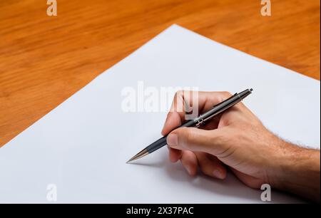 Der Mann beginnt zu schreiben, indem er einen Kugelschreiber auf ein leeres Blatt Papier hält. Hand ist bereit zum Schreiben. Schreibblockade Stockfoto