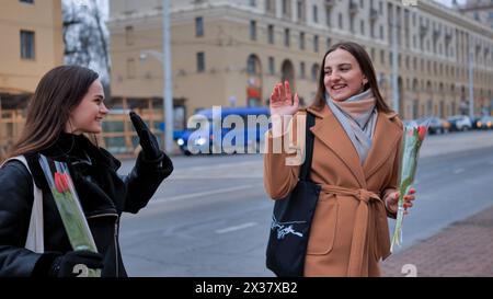 Zwei hübsche junge Frauen mit Blumen in der Hand verabschieden sich Stockfoto