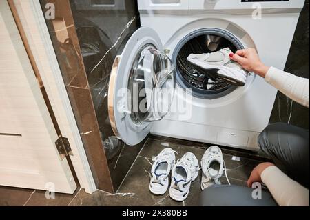 Zugeschnittenes Foto einer Frau, die ihre Schuhe in die Waschmaschine legt. Sportschuhe müssen nach einem langen Workout im Freien gewaschen werden. Stockfoto