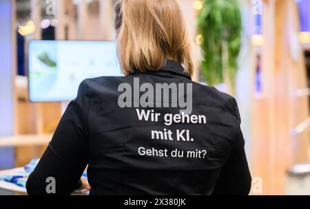 Hannover, Deutschland. April 2024. Eine Frau steht mit einem Hemd, auf dem steht: "Wir gehen mit KI. Gehst du mit uns?“ Auf dem Google-Stand auf der Hannover Messe 2024. Künstliche Intelligenz ist eines der Hauptthemen der Industriemesse. Quelle: Julian Stratenschulte/dpa/Alamy Live News Stockfoto