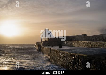 Porthcawl Leuchtturm bei Sonnenaufgang mit einer Welle, die über den Pier kracht. Mid Glamorgan, Großbritannien Stockfoto