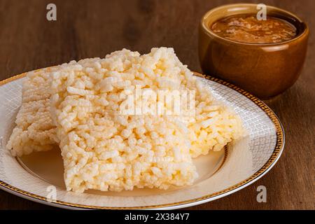 Stapel von quadratischen knusprigen Reiscrackern in wunderschöner brauner Keramikschale mit Erdnusssauce in brauner Keramikschale auf Holztisch. Stockfoto