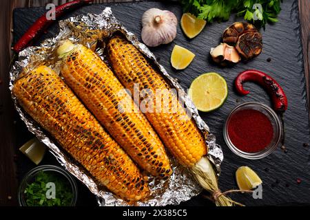 Gegrillter Mais auf dem Kolben in Zinnfolie auf Küchentisch gesund glutenfrei flach legen Lebensmittel Hintergrund Stockfoto