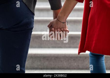 Unerkennbares, junges lateinamerikanisches Paar, das rückwärts geht und Hände hält. Mittlere Nahaufnahme ihrer ineinander verflochtenen Hände. Konzept von Liebe und Relaxatio Stockfoto