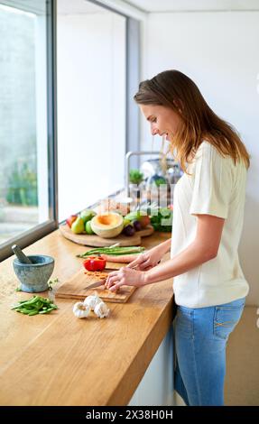 Lächeln, zu Hause und Frau mit Gemüse, Schneiden und Salat mit Bio-Zutaten, gesunde Mahlzeit und Lebensmittel. Wellness, Vegetarier und Person in der Küche Stockfoto