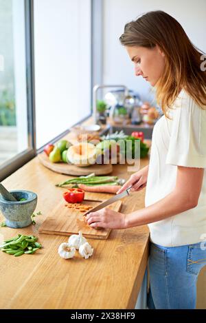 Vegan, zu Hause und Frau mit Gemüse, Schneiden und Essen mit gesunder Mahlzeit, Hobby und Ernährung. Bio-Zutaten, vegetarisch und Person in der Küche Stockfoto