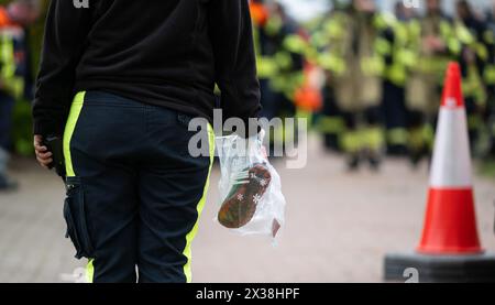 Elm, Deutschland. April 2024. Ein Hundeführer hält eine Tasche mit Kinderschuhen. Freiwillige Feuerwehrleute stehen nach ihrer Mission vor der Essenstheke. Der sechsjährige Arian aus Elm (Bezirk Bremervörde) bleibt am vierten Tag in Folge vermisst. Quelle: Philipp Schulze/dpa/Alamy Live News Stockfoto