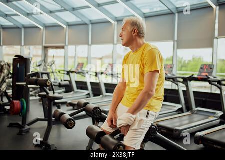 Reifer, sportlicher Mann, der sich während des Trainings im modernen Fitnesscenter in der Nähe von Trainingsgeräten ruht. Stockfoto