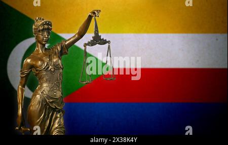 Nahaufnahme einer kleinen Bronzestatuette von Lady Justice vor einer Flagge der Komoren. Stockfoto