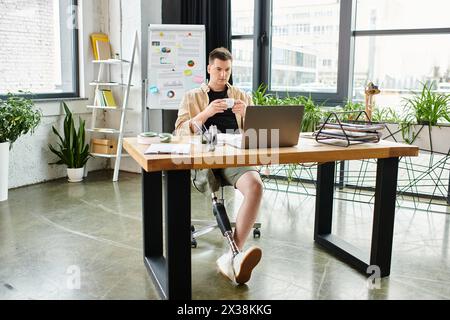 Ein gutaussehender Geschäftsmann mit einer Beinprothese, der fleißig an einem Schreibtisch mit einem Laptop arbeitet. Stockfoto