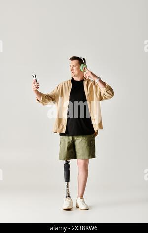 Ein gutaussehender Mann mit einer Beinprothese, trägt ein schwarzes Hemd und khakifarbene Shorts und hält ein Handy. Stockfoto