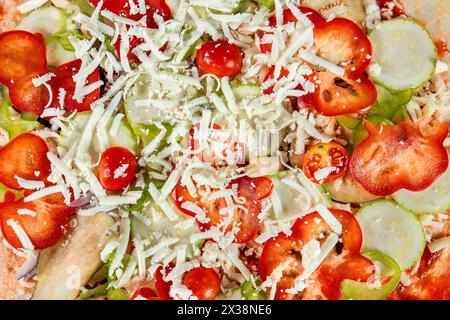 Ein Nahaufnahme einer vegetarischen Pizza vor dem Backen, mit Mozzarella, Tomaten, roten und grünen Paprika und Gurkenscheiben, arran Stockfoto