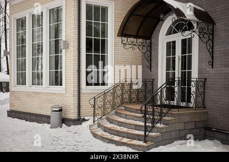 Haus aus Ziegeln, Steintreppen der Veranda mit Metallgeländern und Vordach im Winter. Stockfoto