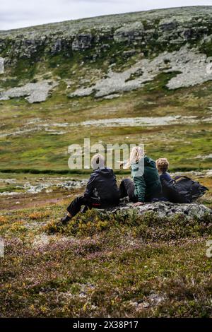 Mutter und zwei Söhne, die sich beim Wandern in der nordischen Landschaft erholen. Die Familie sitzt auf einem Felsen und die Mutter weist auf etwas in der Ferne hin. Stockfoto