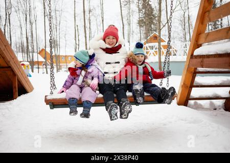 Mutter mit zwei Kindern auf Schaukel am Wintertag. Stockfoto