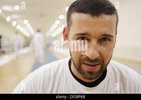 Gutaussehender Mann in weißen Posen im Fitnessstudio, andere Leute außer Fokus Stockfoto