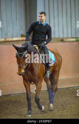 Ein schöner Mann in Schwarz reitet braunes Pferd im Hartzeug im hippodrom Stockfoto