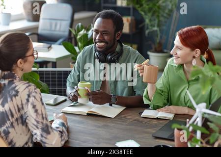 Multiethnisches Team aus lächelnden jungen Geschäftsleuten, die im Büro arbeiten und am Meeting-Tisch im grünen Büro sitzen Stockfoto