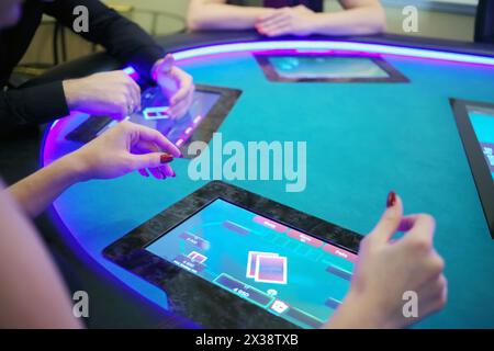 Hände von zwei Frauen und Männern spielen Poker im Casino mit elektronischem Tisch, Fokus auf Frauenhand Stockfoto