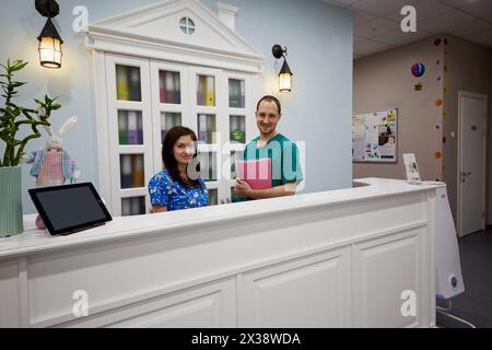 Ärztin und Registerin weibliche Mitarbeiterin an der Rezeption des Kinderkrankenhauses für Kinder aller Altersgruppen von der Geburt bis zum 17. Lebensjahr. Stockfoto