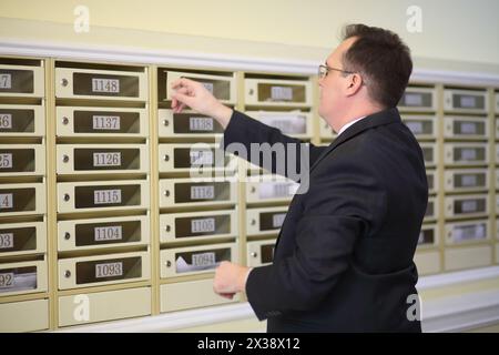 Ein Mann in einem Business-Anzug öffnet den Briefkasten in der Lobby des Appartementgebäudes Stockfoto