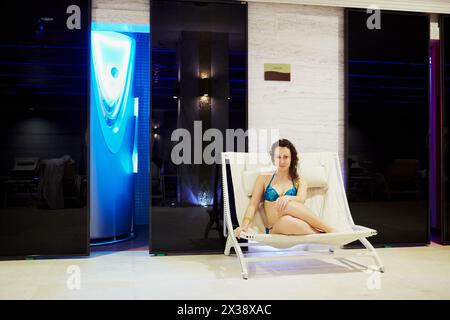 MOSKAU, RUSSLAND - 14. November 2015: Junge Frau in Badeanzügen sitzt auf einer Lounge unter einem Teller mit Solarium-Aufschrift im Erholungsgebiet in Radisson Royal UK Stockfoto