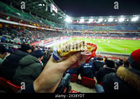 Burger in der Hand und steht während des Fußballspiels im Stadion am Abend Stockfoto