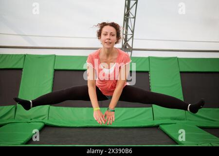 Junge Frau springt auf Trampolin und macht einen Spliss. Stockfoto