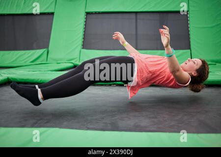 Junge Frau springt auf Trampolin-Attraktion in liegender Position. Stockfoto