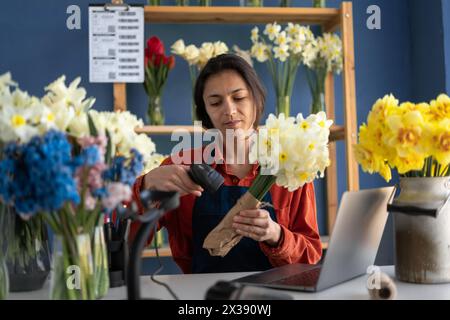 Floristik-Konzept. Wunderschöne hispanische Unternehmerin, die in einem eigenen Blumenladen arbeitet und Blumenstrauß herstellt. Die Frau macht in ihrem Laden Blumen. Stockfoto