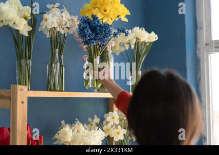 Eine Floristin, die eine Vase mit Blumen auf ein Regal legt, während sie in ihrem Blumenladen arbeitet. Stockfoto