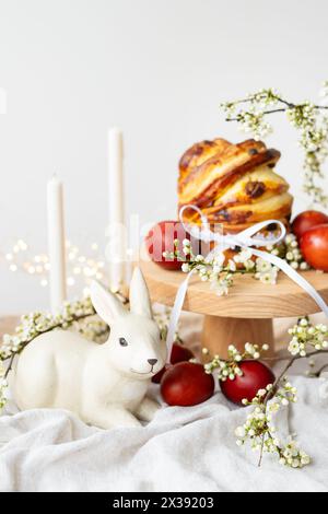 Festlicher Tisch mit Keramikhase, roten Eiern, Kerzen und Ostergebäck, vertikales Foto. Osterferienkonzept Stockfoto