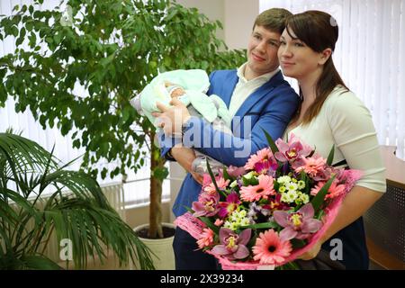 Junger Mann, Frau mit Blumen und kleines Baby in der Decke steht in der Entbindungsklinik Stockfoto