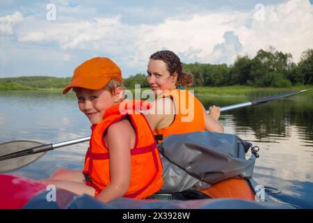 Kleiner Junge und Frau in Schwimmwesten segeln im Sommer auf einem Schlauchboot auf dem Fluss, konzentrieren Sie sich auf die Frau Stockfoto