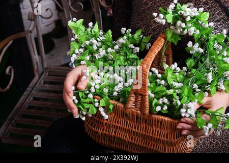 Frau im Kleid hält Korb mit Blumen auf Eisenbank im Studio, Nahaufnahme Stockfoto