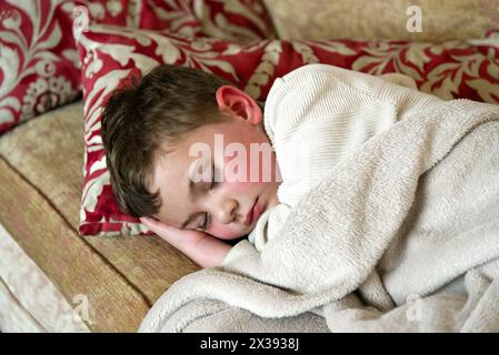 Ein junger 5-jähriger Junge, der auf einer Couch schlief und seinen Kopf auf der Hand liegend Stockfoto