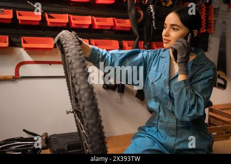 Frau Mechanikerin, die mit dem Kunden telefoniert und beschädigtes Motorrad repariert Stockfoto