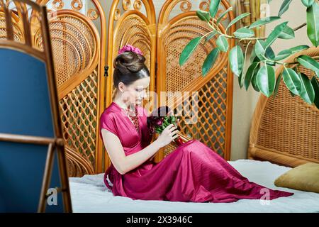 Eine junge Frau mit einem Blumenstrauß sitzt auf einem Korbbett. Stockfoto