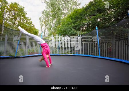 Junge glückliche Frau springt draußen auf schwarzem Trampolin am Sommertag Stockfoto