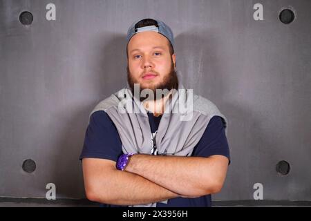 Ein schöner feiner Mann mit Bart posiert mit überkreuzten Armen im Studio nahe der Wand Stockfoto