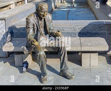 Craiova, Rumänien - 16. März 2024: Bronzestatue des alten Mannes, der Tauben und Tauben füttert, auf einer Bank im Stadtzentrum am sonnigen Frühlingstag. Stockfoto