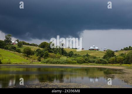 Sturmwolken, unheilvoller Himmel, Hügel und Kirche, grüne Bäume vor dem Regen. Stockfoto