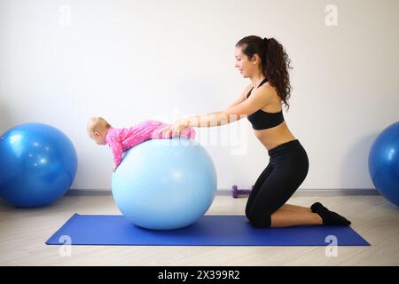 Mutter und Baby machen Übungen auf dem großen blauen Ball im Fitnessstudio Stockfoto